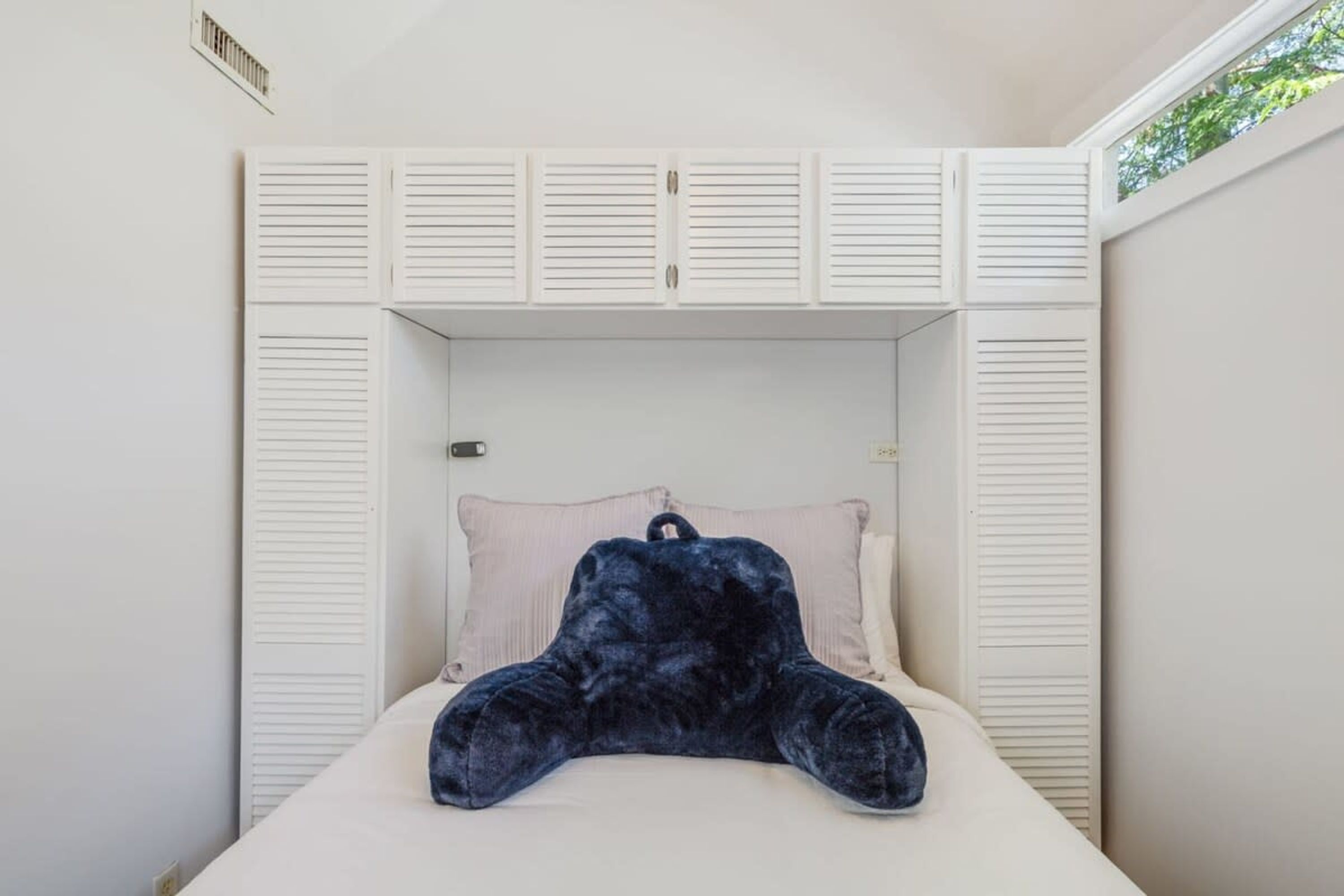 Een slaapkamer met een bed, een donzig kussen in donkerblauw en witte louvre-kasten.