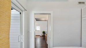 Ein schmaler Flur mit einem Bett auf der rechten Seite, einer Tür am Ende und einer Pflanze in der Mitte.