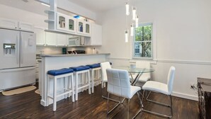 Eine moderne Küche mit weißen Schränken, einer zentralen Kochinsel mit Barhocker und einem Essbereich mit Glastisch und weißen Stühlen.