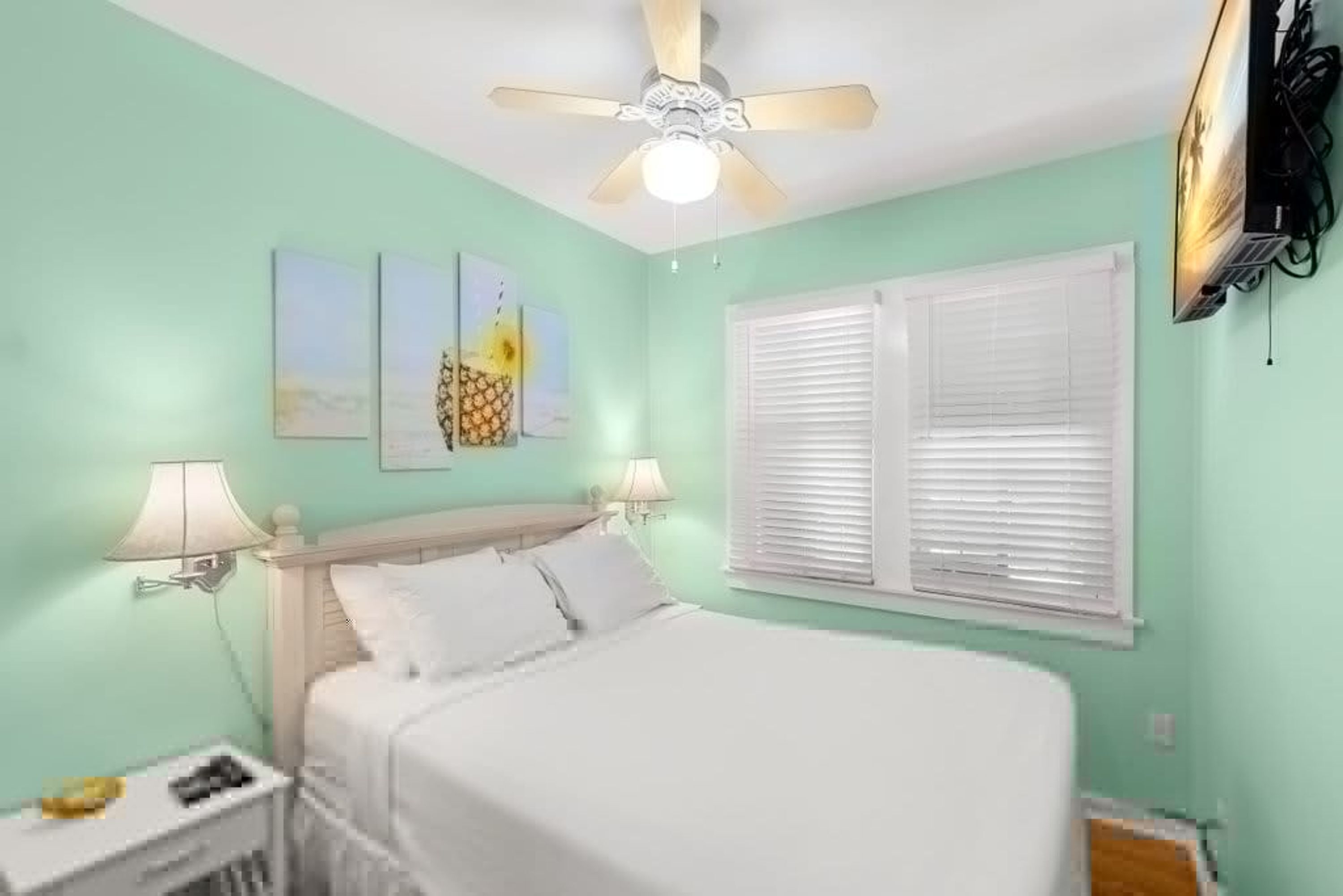 Une chambre à coucher avec un lit, deux lampes fixées au mur, un ventilateur de plafond et une fenêtre avec des stores.