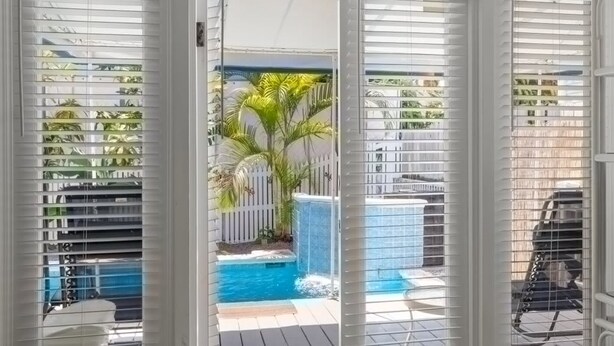 A pool area with a waterfall feature, surrounded by palm trees and a white fence. - Poolside Paradise by Brightwild Heated Pool (Key West)