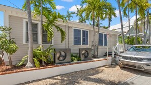 A mobile home with two air conditioning units, a white car parked in front, and palm trees around. - Poolside Paradise by Brightwild Heated Pool (Key West)