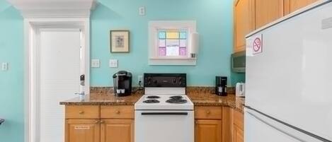 Une cuisine avec un four blanc, des meubles en bois, un réfrigérateur blanc et un mur de couleur turquoise.