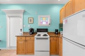 A kitchen with a white stove, wooden cabinets, a white refrigerator, and a teal wall.