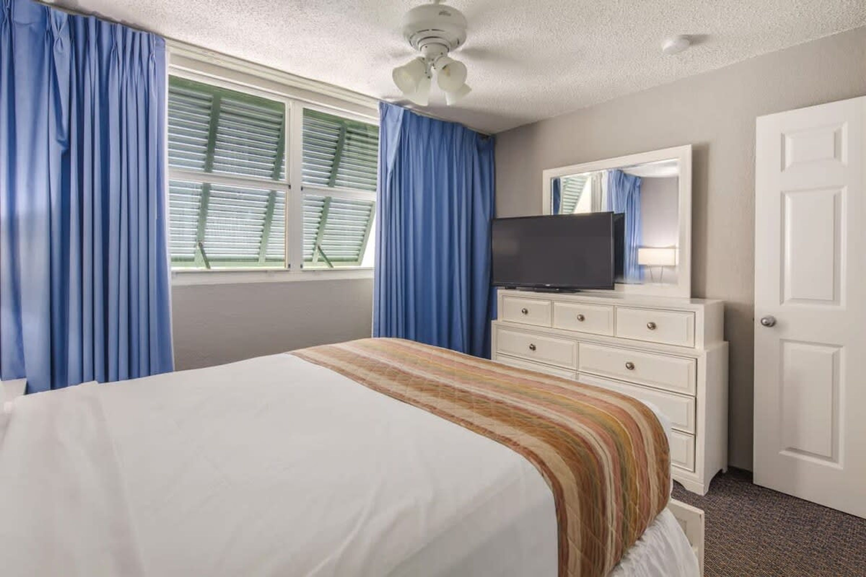 A hotel room with a bed, a dresser, a television, and a door.