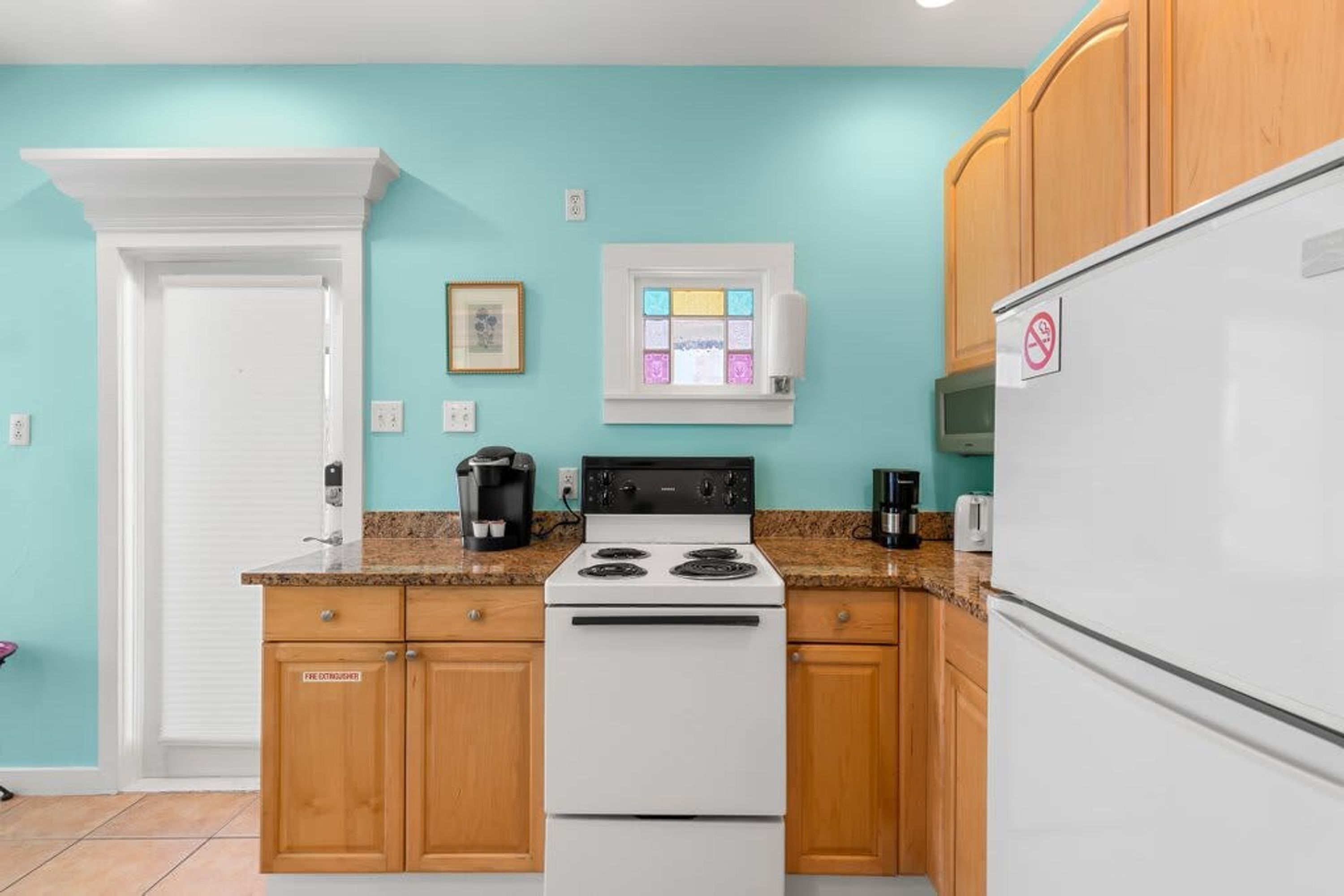 Una cocina con paredes azul verdoso, gabinetes de madera, una estufa blanca y un refrigerador blanco.