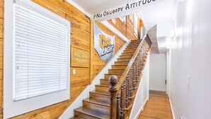 A wooden staircase with a Coors Light banner, a white door, and a sign stating 'No Grumpy Attitude'.