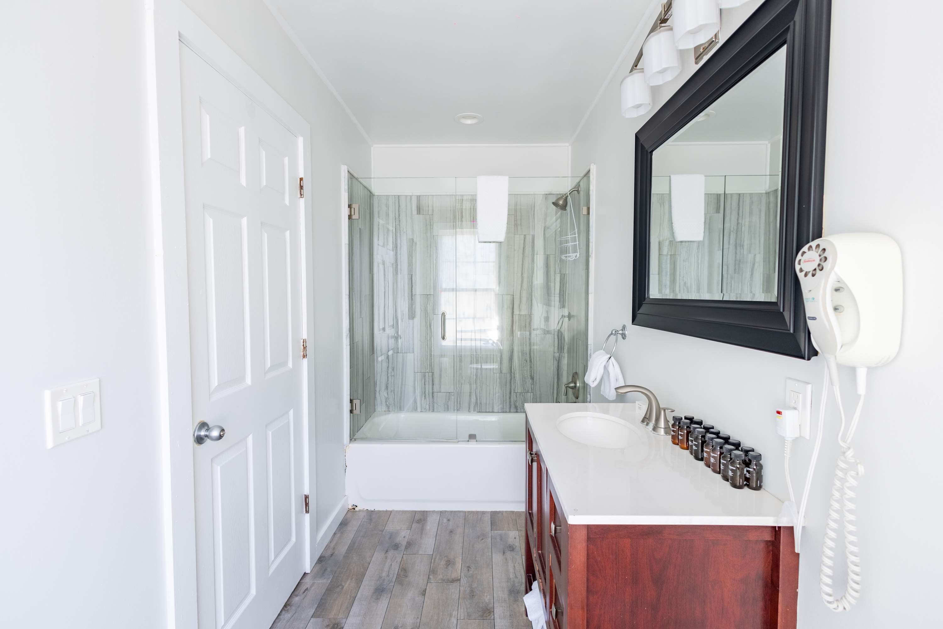 A bathroom with a glass shower enclosure, a white bathtub, a vanity with a mirror, and a white telephone.