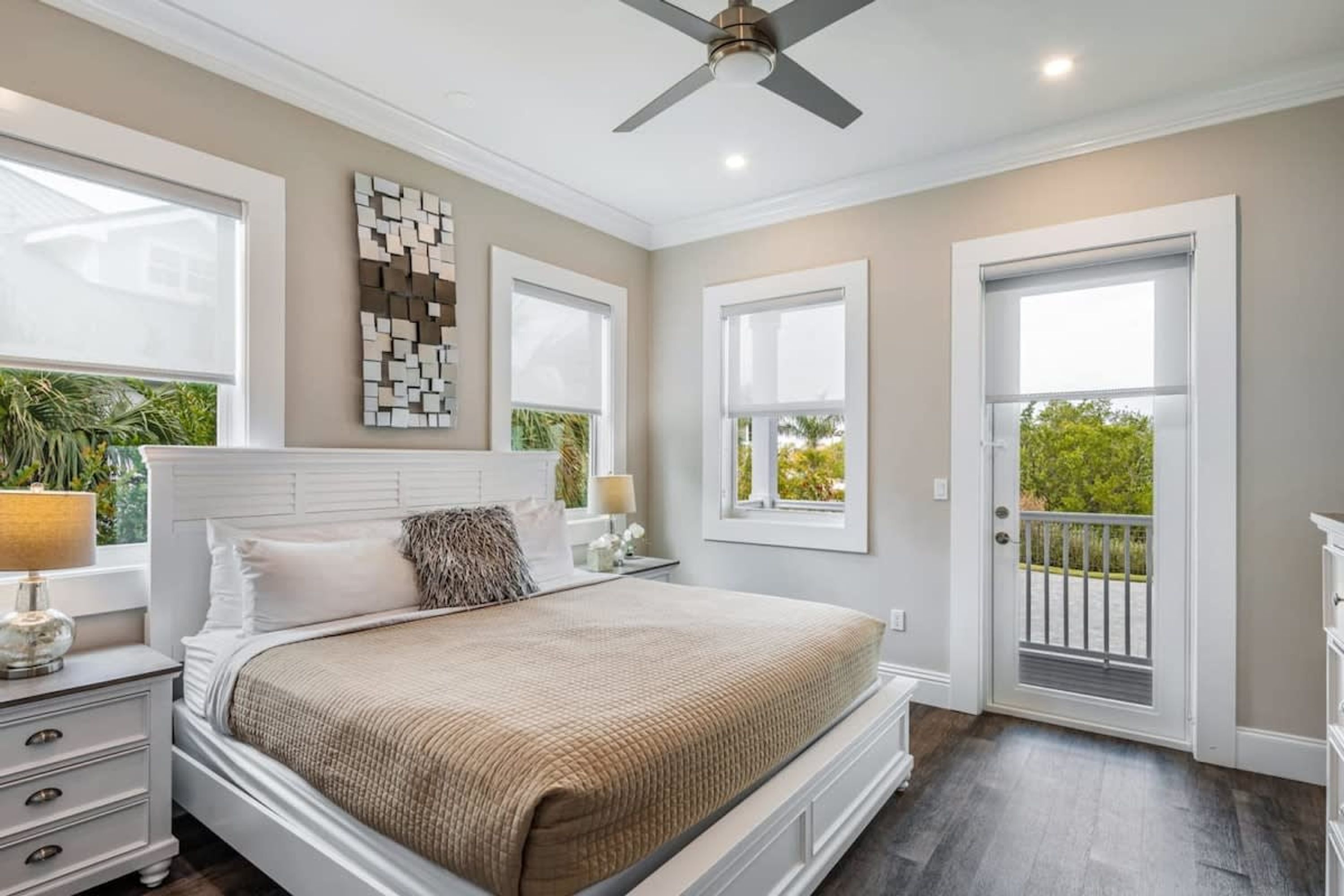 A bedroom with a bed, nightstands, a ceiling fan, and a view of greenery outside.