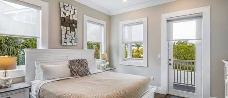 A bedroom with a bed, nightstands, a ceiling fan, and a view of greenery outside.