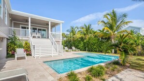 Un espace piscine doté d’une terrasse couverte, de palmiers et d’une maison avec un balcon.