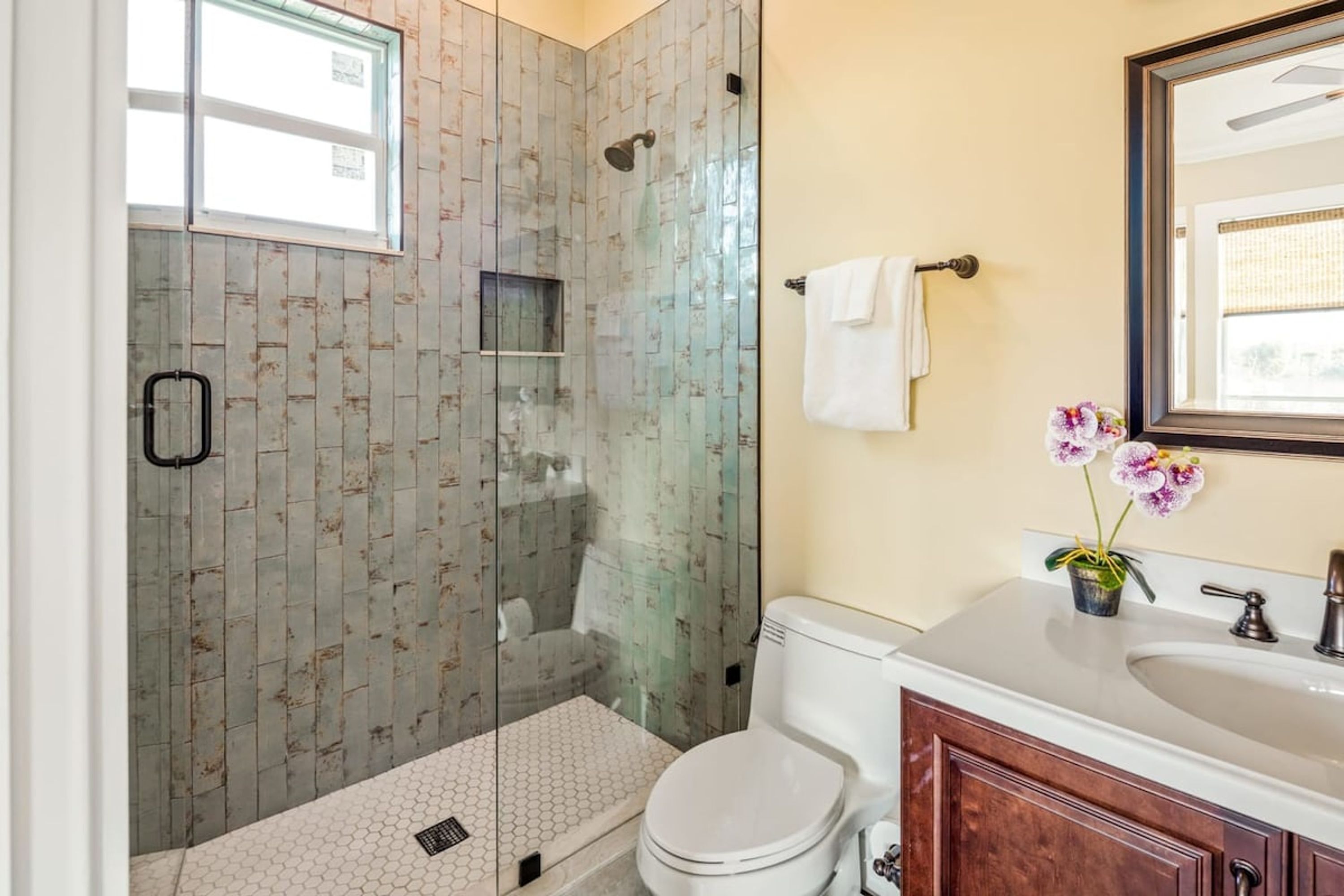 A bathroom with a glass-enclosed shower, a toilet, a sink, and a mirror.