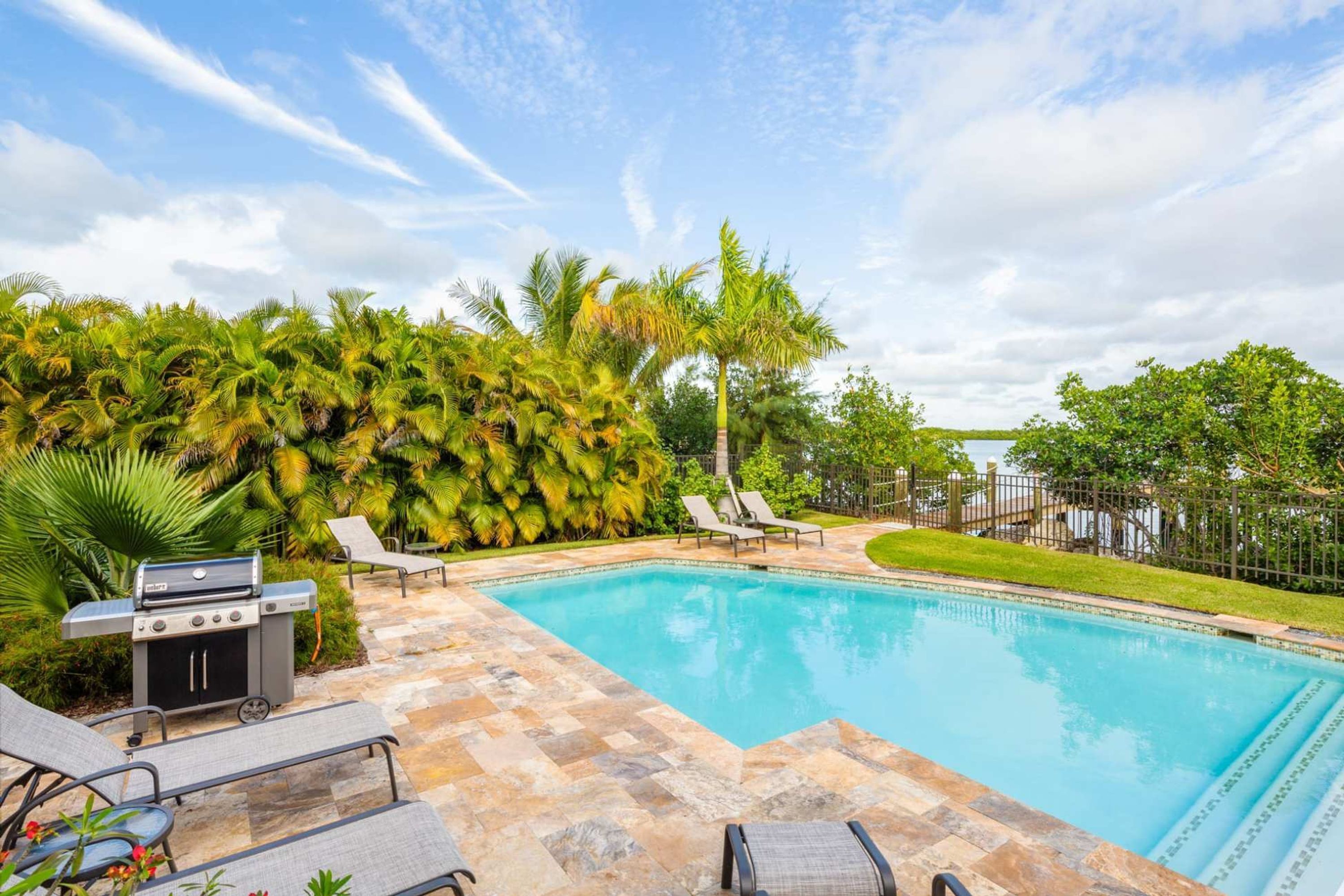 Una piscina con lettini e zona barbecue, circondata da palme e vista sull'acqua.