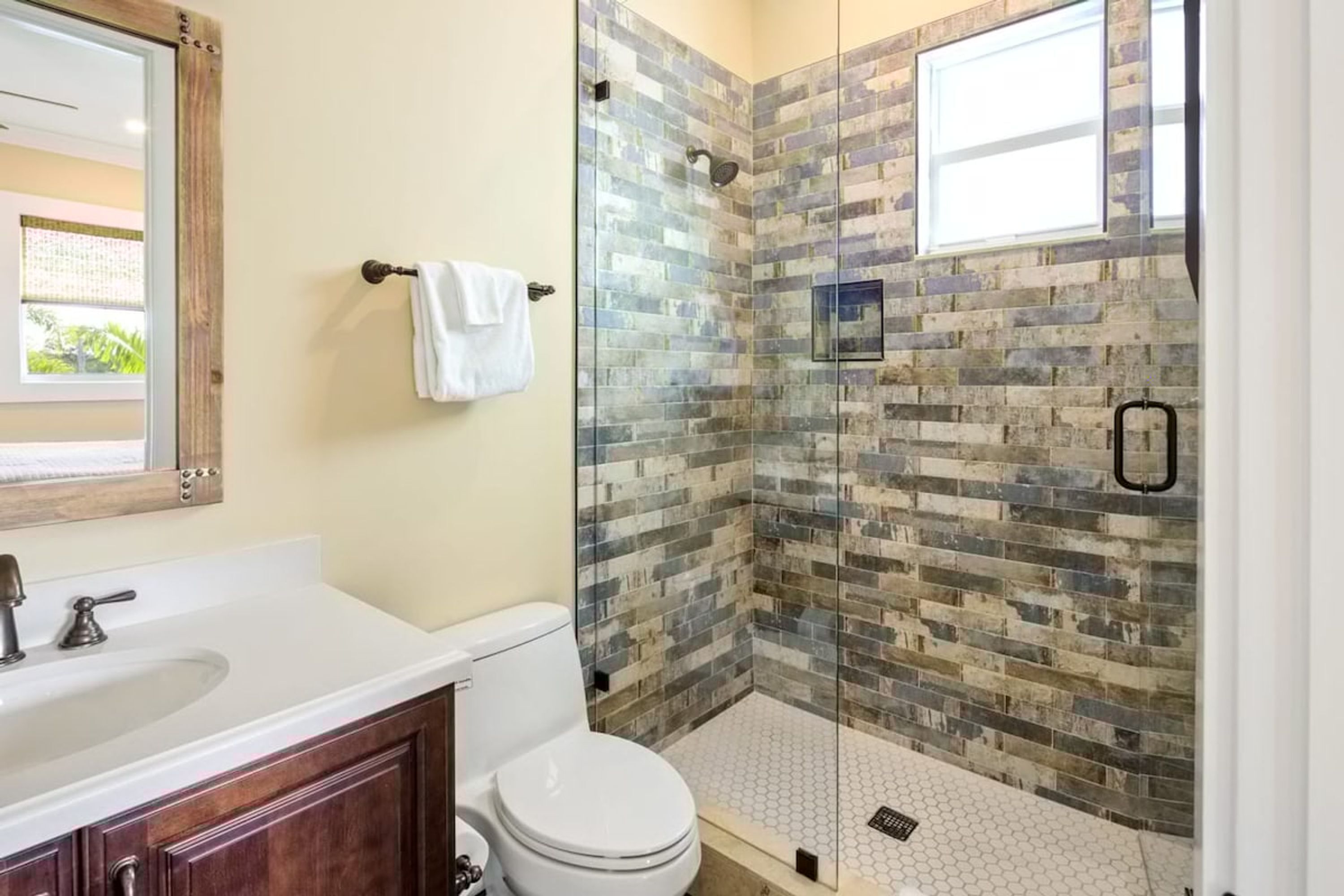 A bathroom with a white sink, a toilet, and a glass-enclosed shower with a mosaic tile wall.