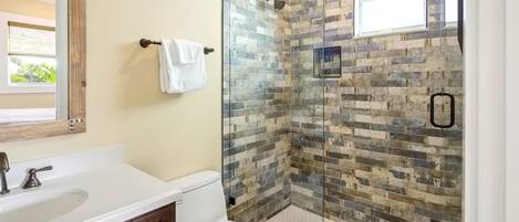 A bathroom with a white sink, a toilet, and a glass-enclosed shower with a mosaic tile wall.