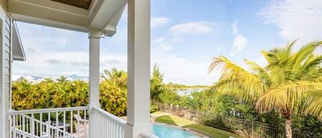 A balcony with a view of a swimming pool, palm trees, and a fenced yard.