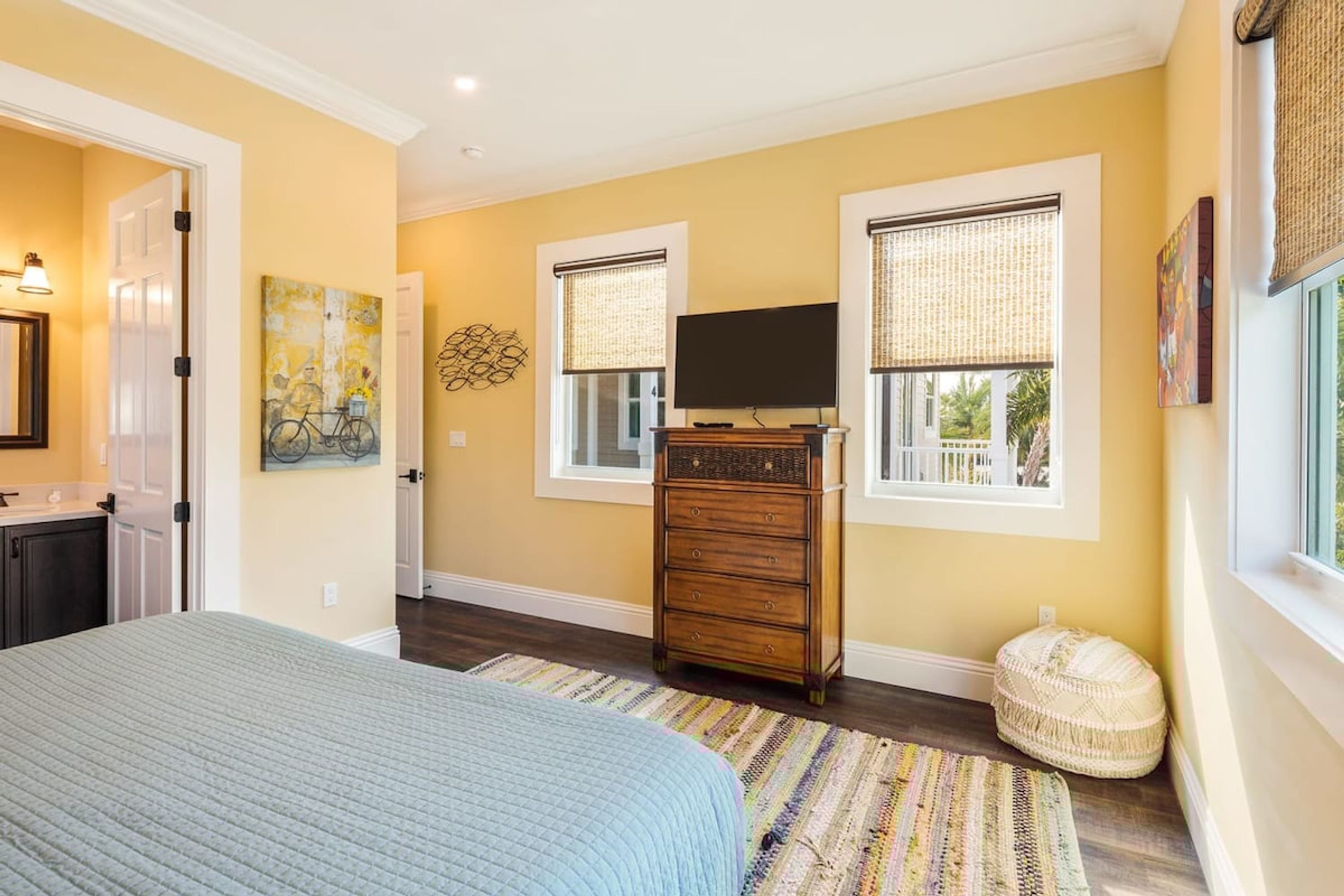 A bedroom with a bed, dresser, TV, and windows with blinds.