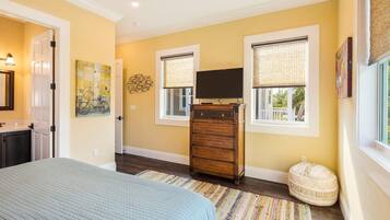 A bedroom with a bed, dresser, TV, and windows with blinds.