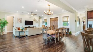 A spacious living area with a wooden dining table, comfortable seating, a flat-screen TV, and a ceiling fan. - Capmar House by Brightwild Huge Home Pool (Key West)