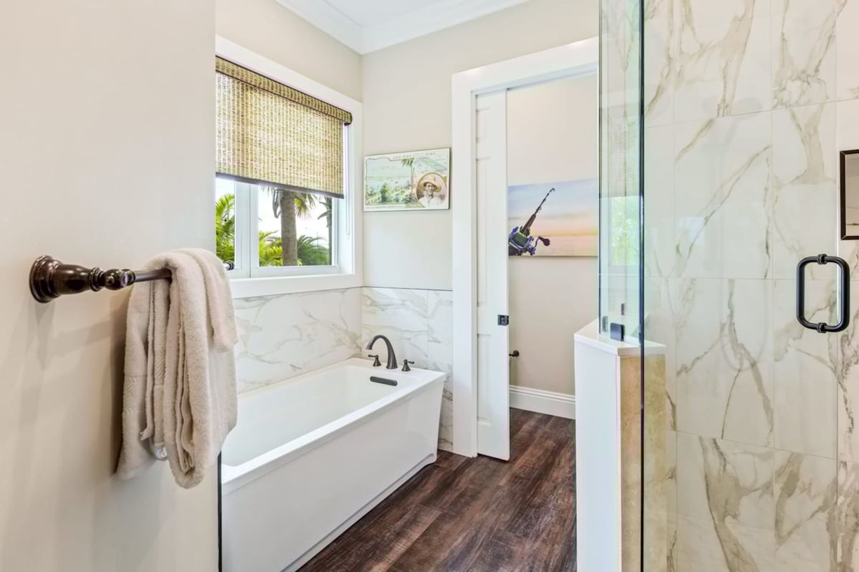 Une salle de bain moderne avec une baignoire blanche, une fenêtre dotée d’un store en bambou et une cabine de douche en verre.