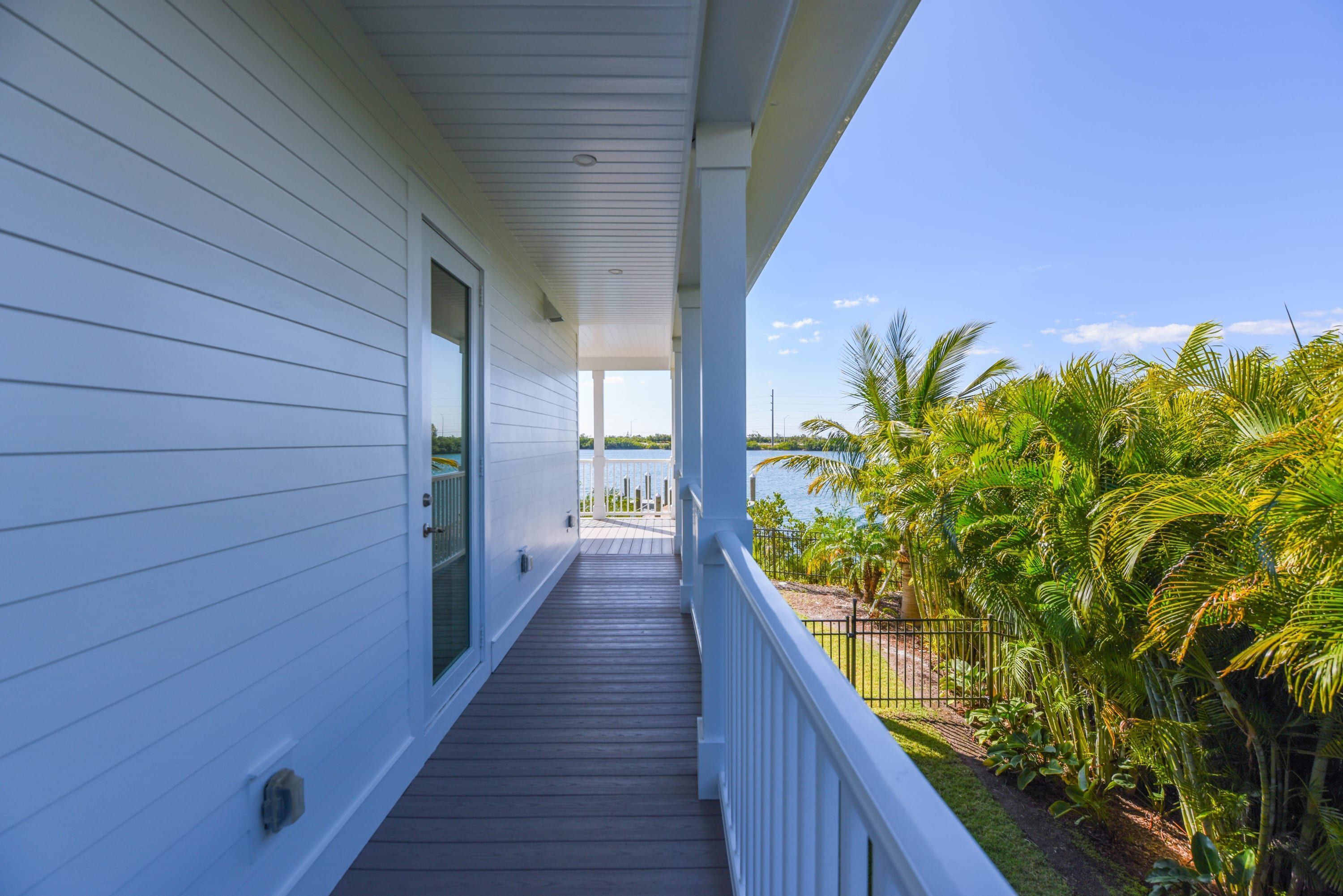 A wooden deck leading to a covered porch with a view of a lush garden and the ocean.
