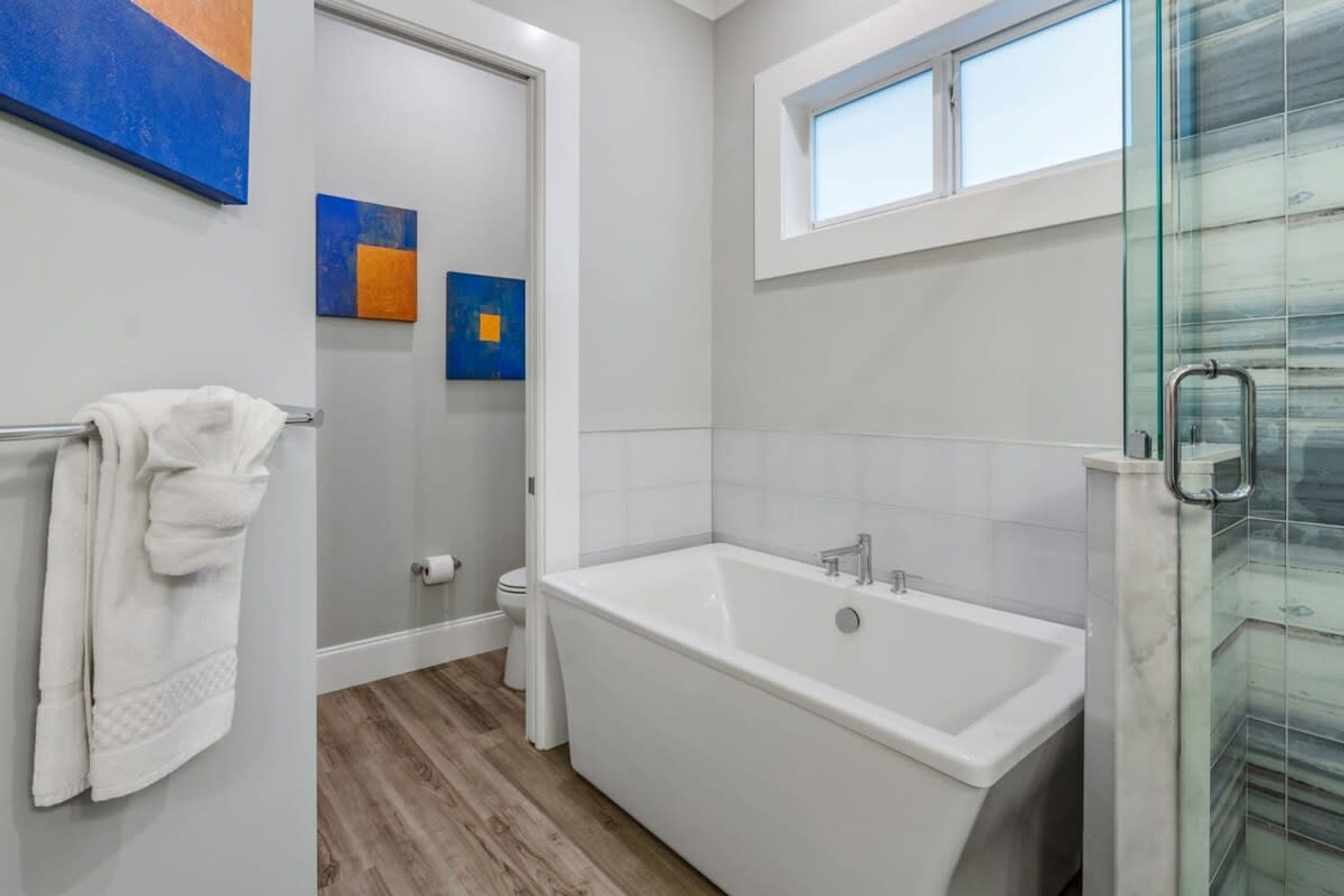 A modern bathroom with a large bathtub, a glass shower enclosure, and a small window above the sink.