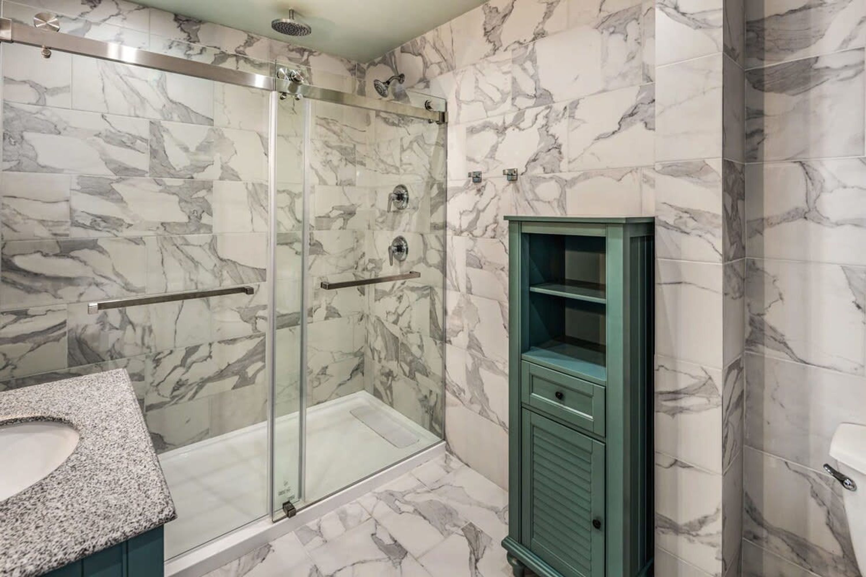 Une salle de bain dotée d’une douche à parois de verre, de murs en marbre et d’un meuble vert.