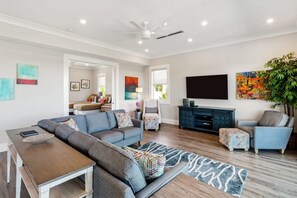A modern living room with a sectional sofa, a coffee table, a TV, and a bookshelf. - Spindrift House by Brightwild Huge Pool Dock (Key West)