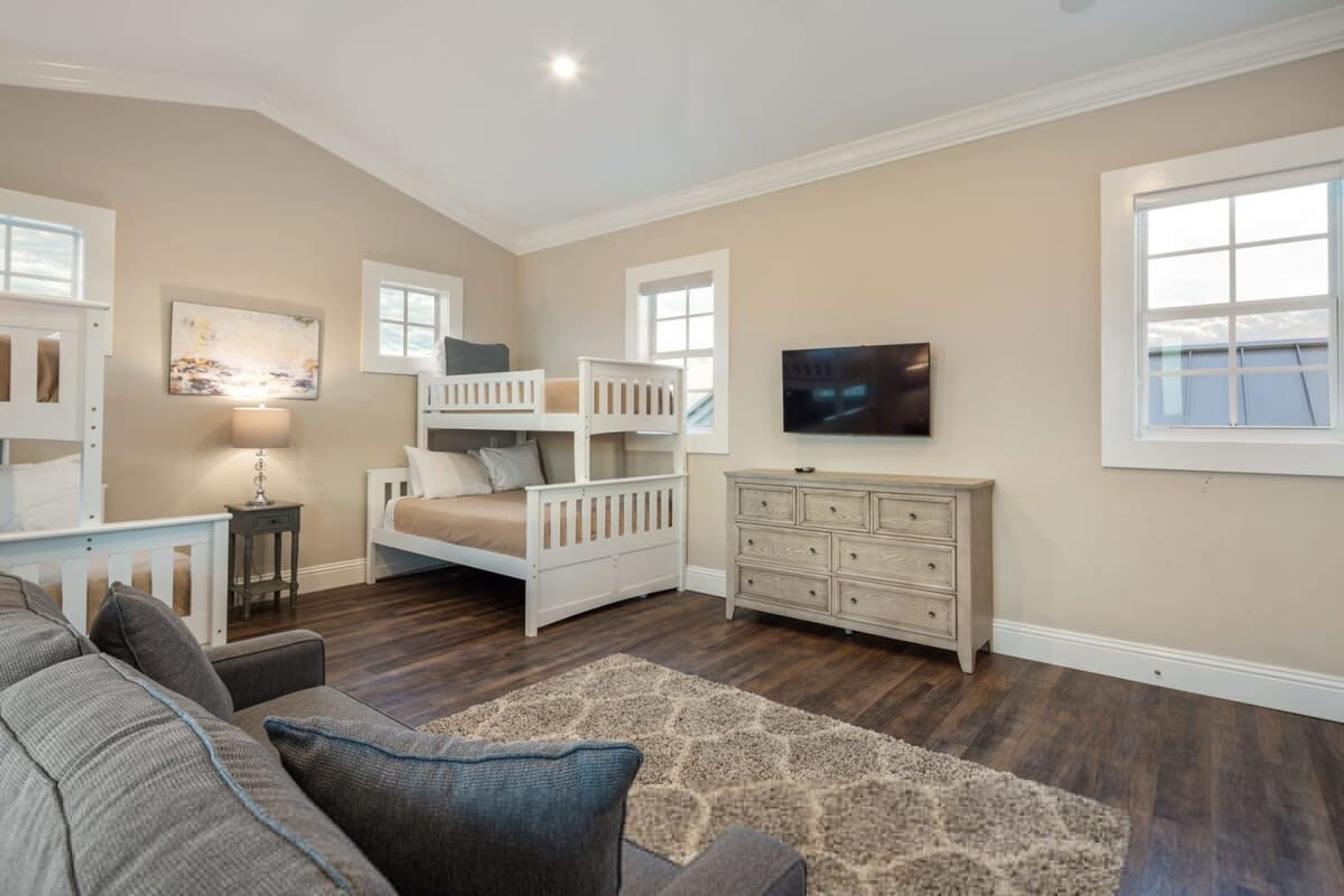 A bedroom with a bunk bed, a dresser, a TV, and a window.