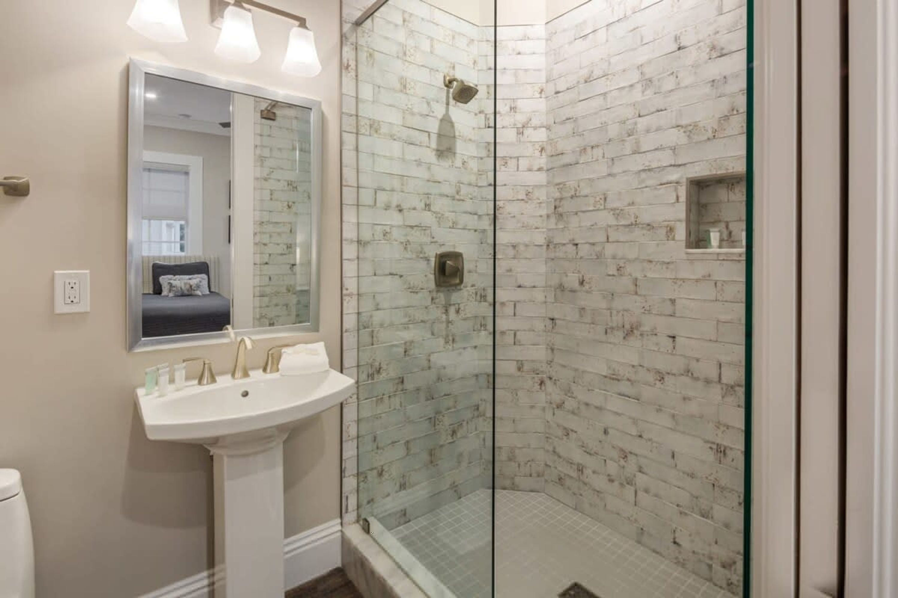 A bathroom with a glass-enclosed shower, a pedestal sink, and a mirror above it.