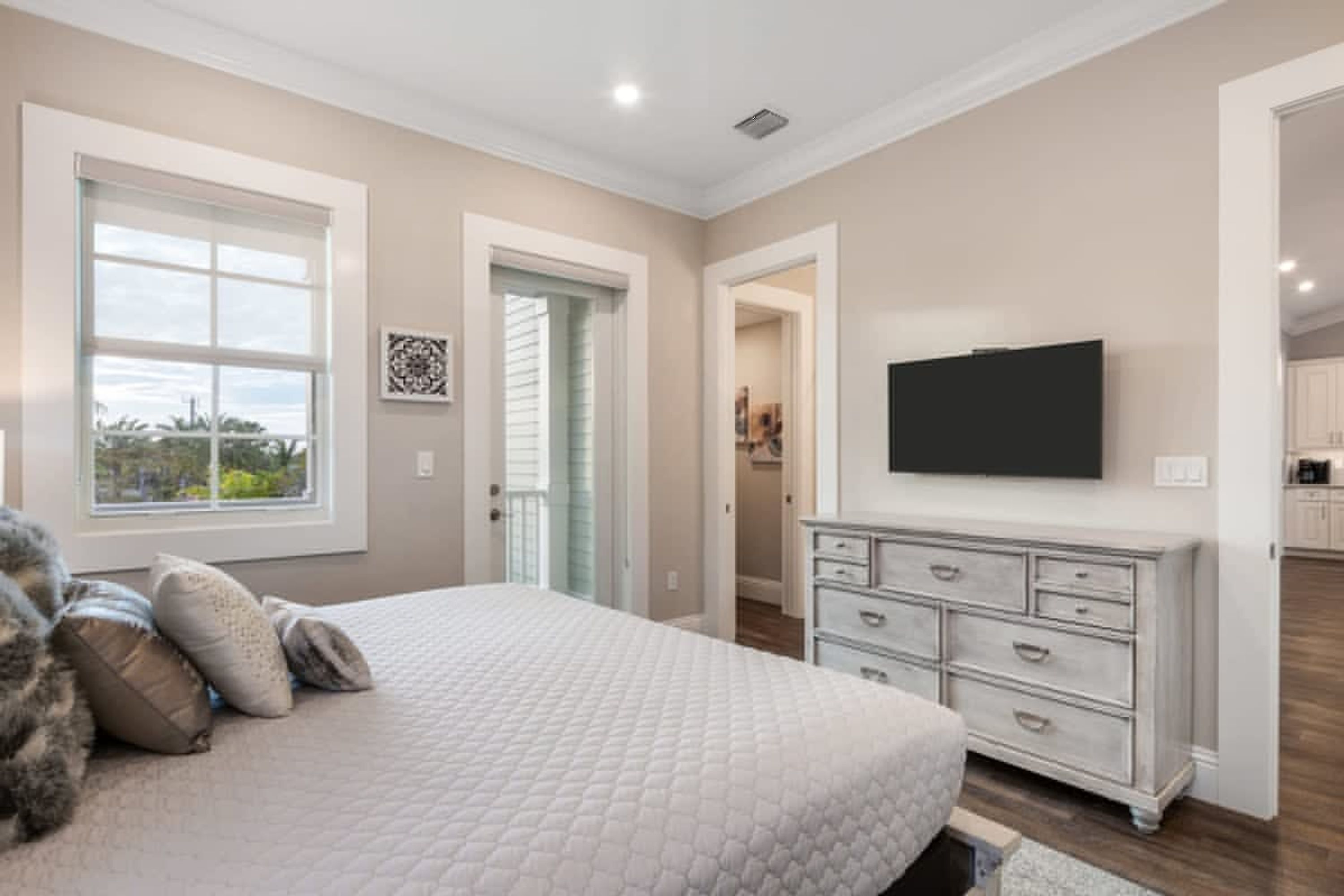 A bedroom with a large bed, a dresser, and a TV mounted on the wall.