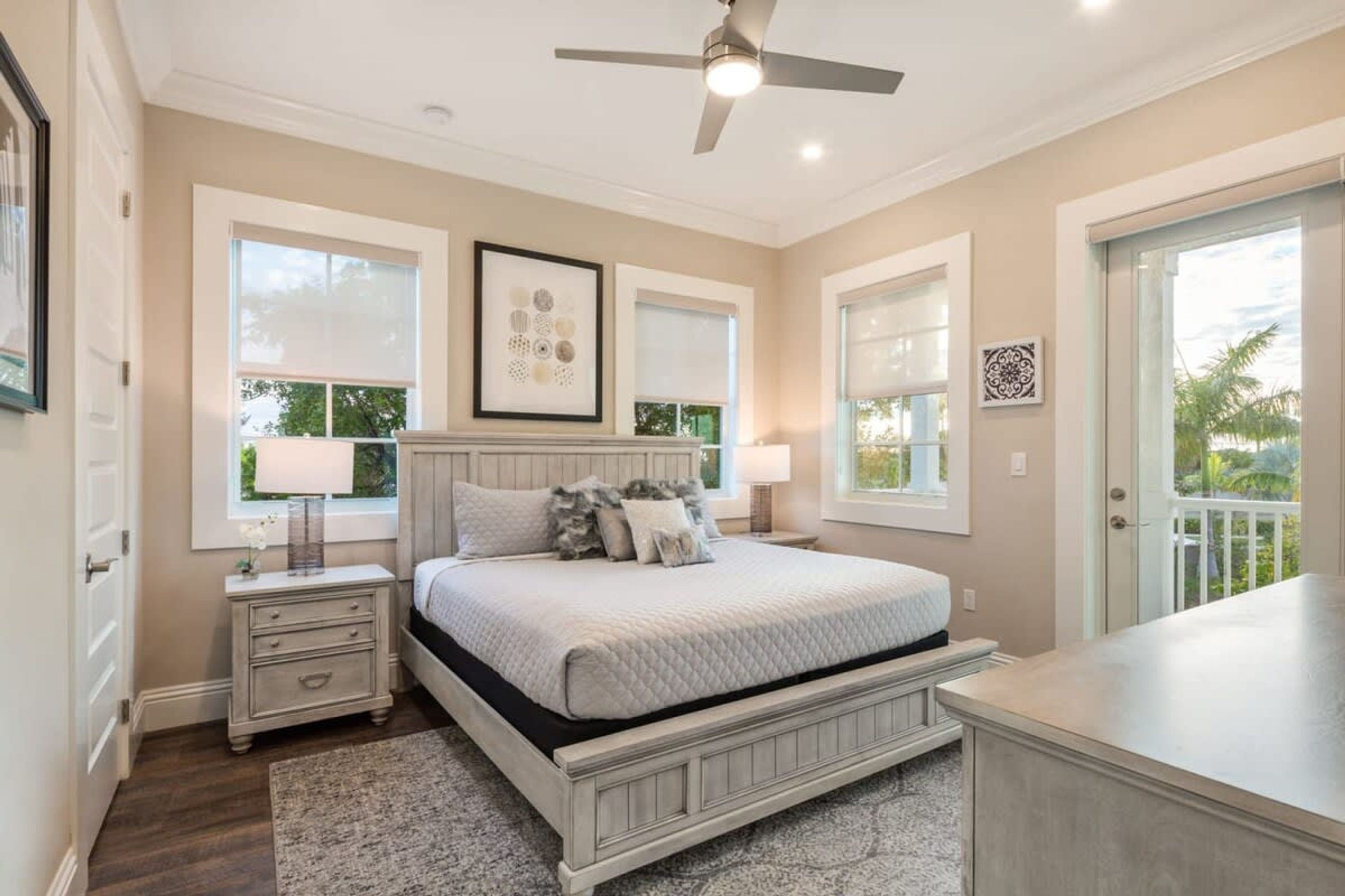 A bedroom with a bed, nightstands, a ceiling fan, and large windows.
