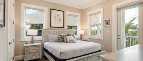 A bedroom with a bed, nightstands, a ceiling fan, and large windows.