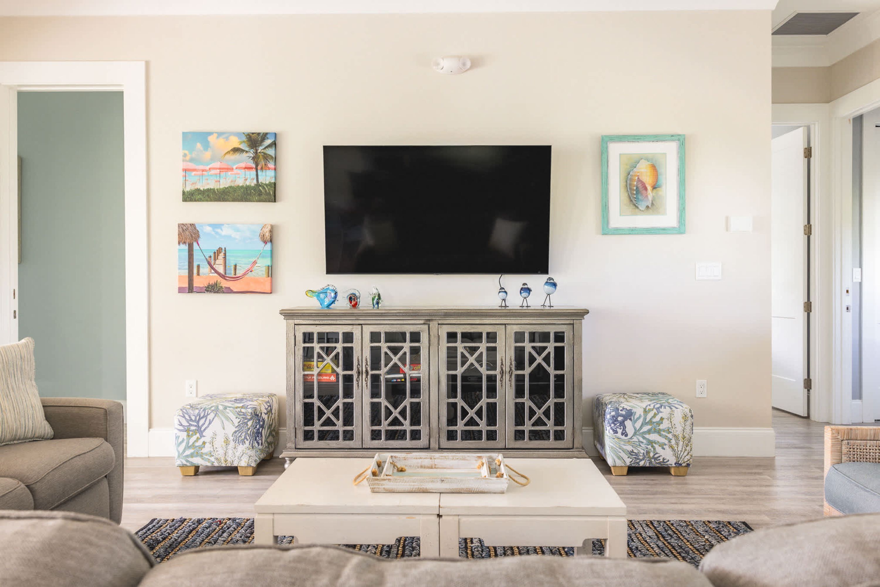 A living room with a flat-screen TV, two framed artworks, a cabinet with glass doors, and a coffee table.
