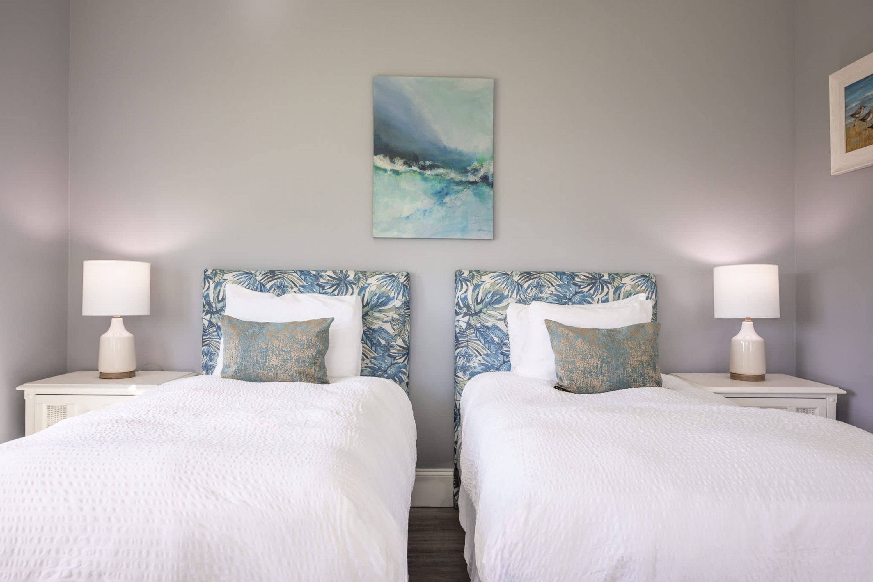 A hotel room with two beds, each with a matching headboard and pillow, white bedding, and a painting on the wall.