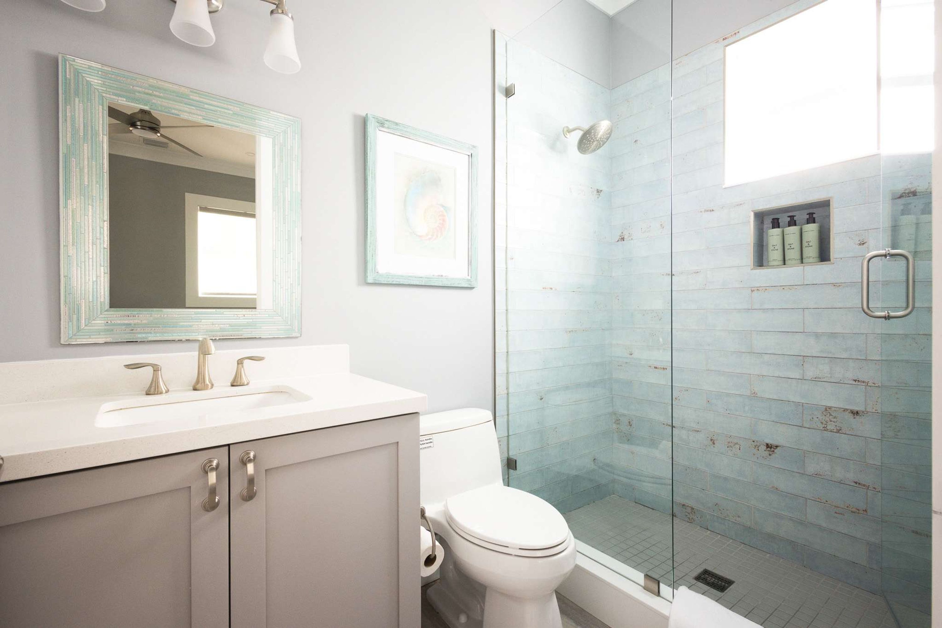 A bathroom with a glass shower enclosure, a white sink, and a framed mirror.