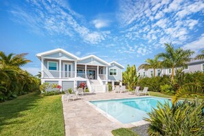 Une maison à deux étages avec une piscine, entourée de palmiers et d’une pelouse bien entretenue.