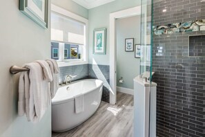 Une salle de bain moderne avec une baignoire sur pieds, une douche à parois de verre et une fenêtre laissant entrer la lumière naturelle.