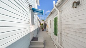 A narrow, white wooden corridor with steps leading to a door, flanked by buildings with green shutters and a blue awning. - Cloud Suite on Duval Luxury Condo Epic Location (Key West)