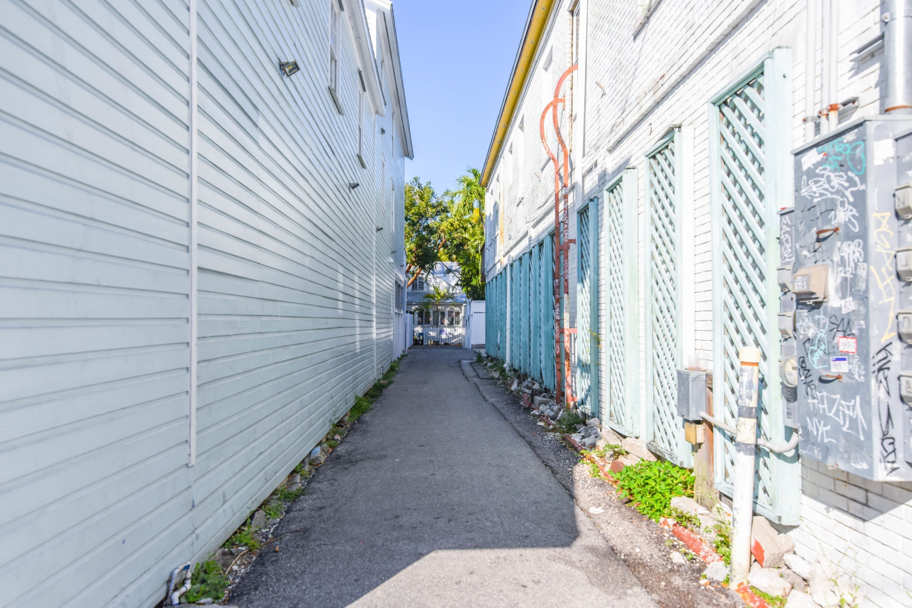 A narrow alleyway flanked by buildings with white siding and green shutters.