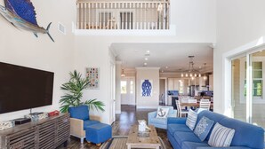 A spacious living room with a large TV, blue sofas, and a wooden coffee table. - Suncoast House by Brightwild Pool Boat Dock (Key West)