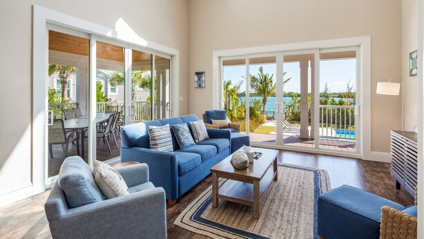 A spacious living area with a blue sofa, a grey armchair, and a wooden coffee table. Large sliding glass doors lead to a pool and outdoor furniture. - Suncoast House by Brightwild Pool Boat Dock (Key West)