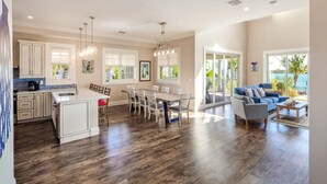 A spacious living area with a dining table and chairs, a kitchen with white cabinets, and a large window overlooking a scenic view. - Suncoast House by Brightwild Pool Boat Dock (Key West)