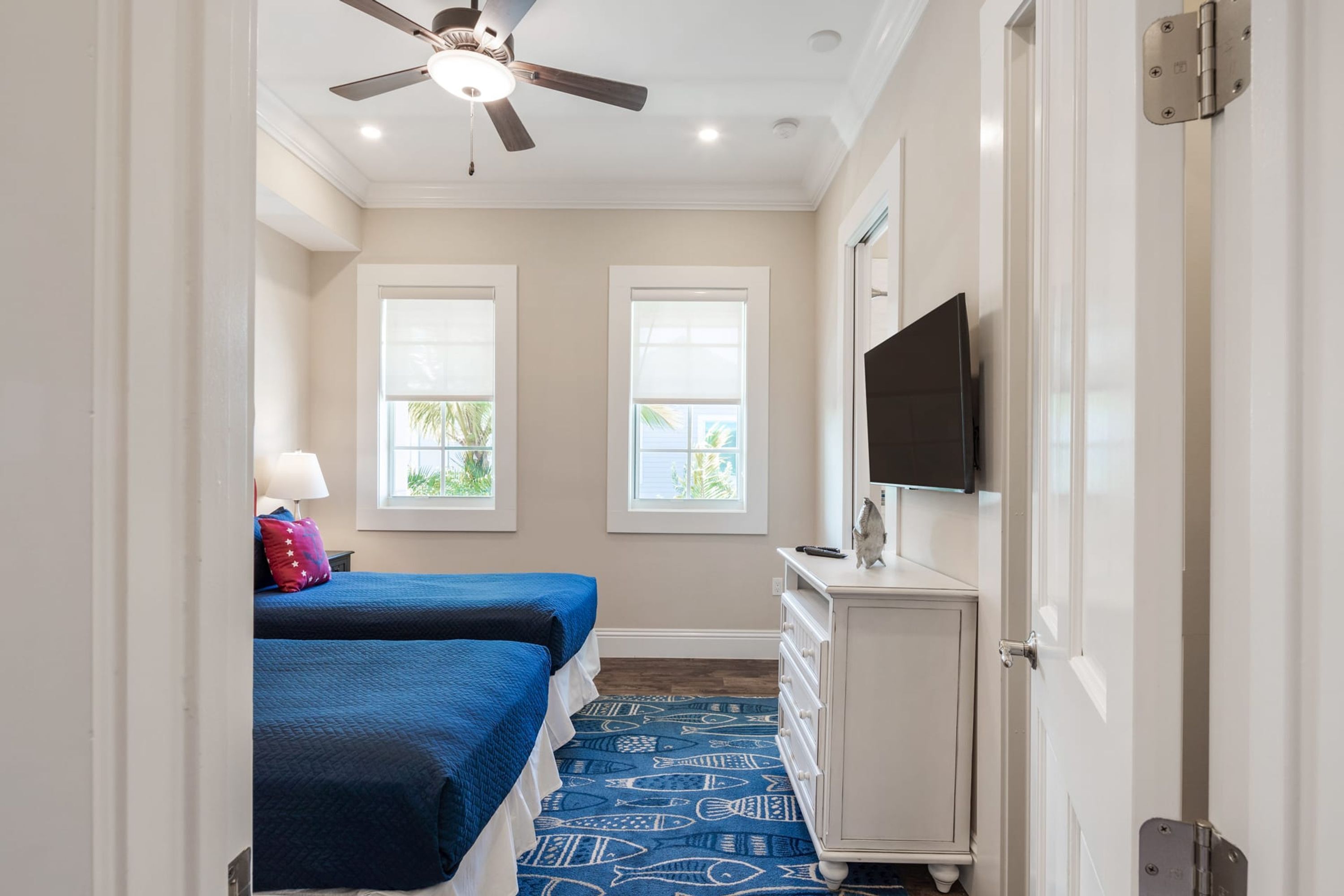 A bedroom with two beds, a ceiling fan, a TV, and a dresser.