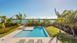 A rectangular swimming pool with clear blue water, surrounded by a paved deck. There are lounge chairs and a small table on the deck. Palm trees and a grassy area are visible in the background. - Suncoast House by Brightwild Pool Boat Dock (Key West)