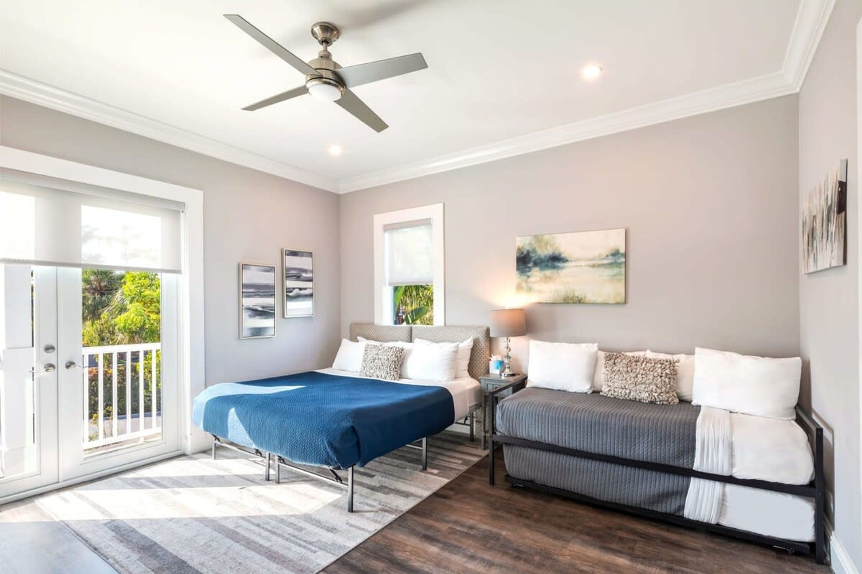A bedroom with a bed, a sofa, a ceiling fan, and artwork on the walls.