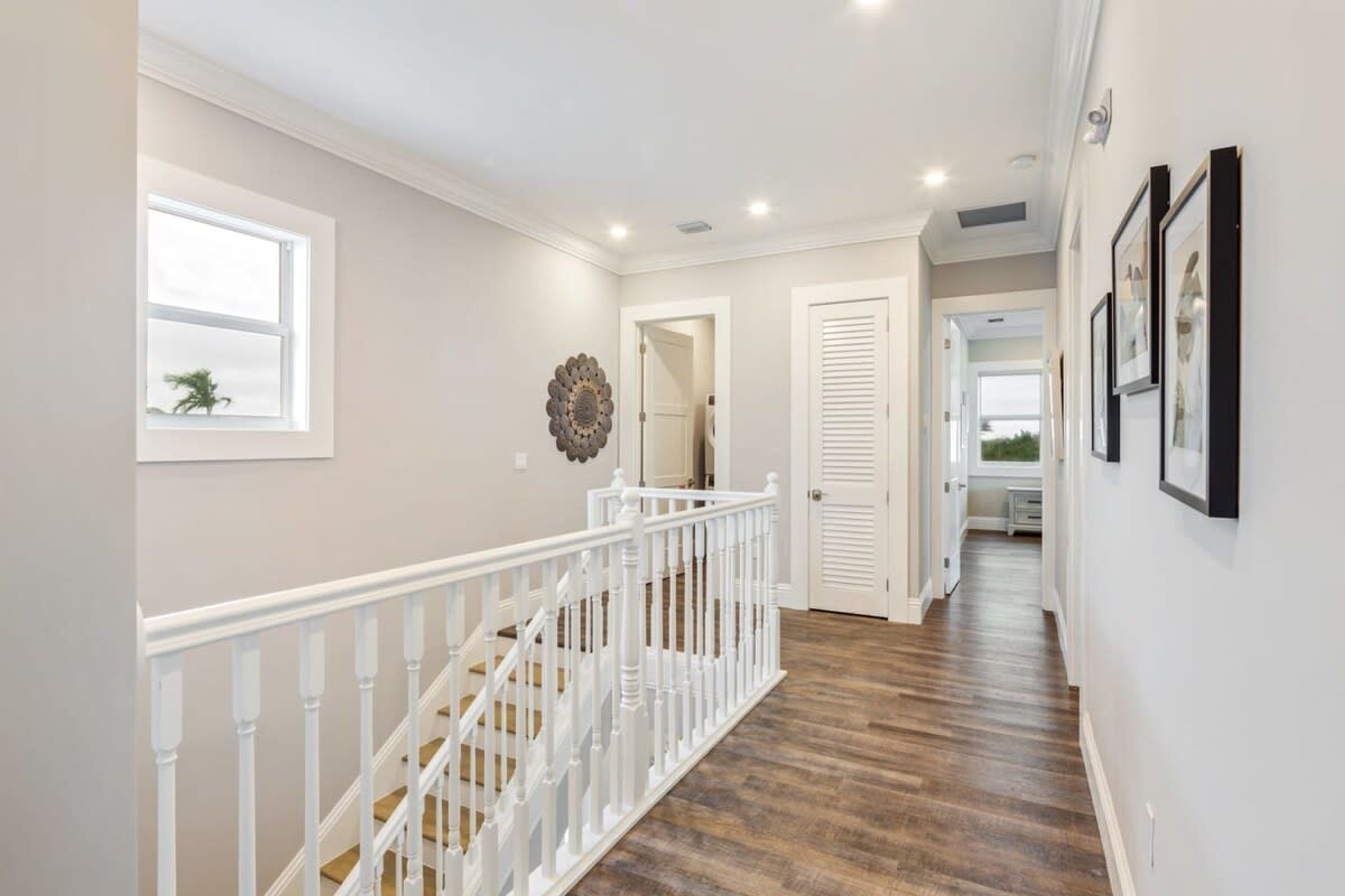 A hallway with a wooden floor, white railing, and a door with louvered shutters.