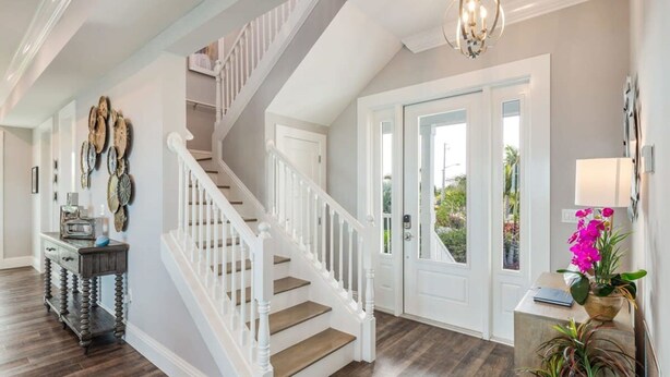 Een ruime hal met een houten trap, een console tafel met decoratieve objecten, en uitzicht op de omgeving door een glazen deur.