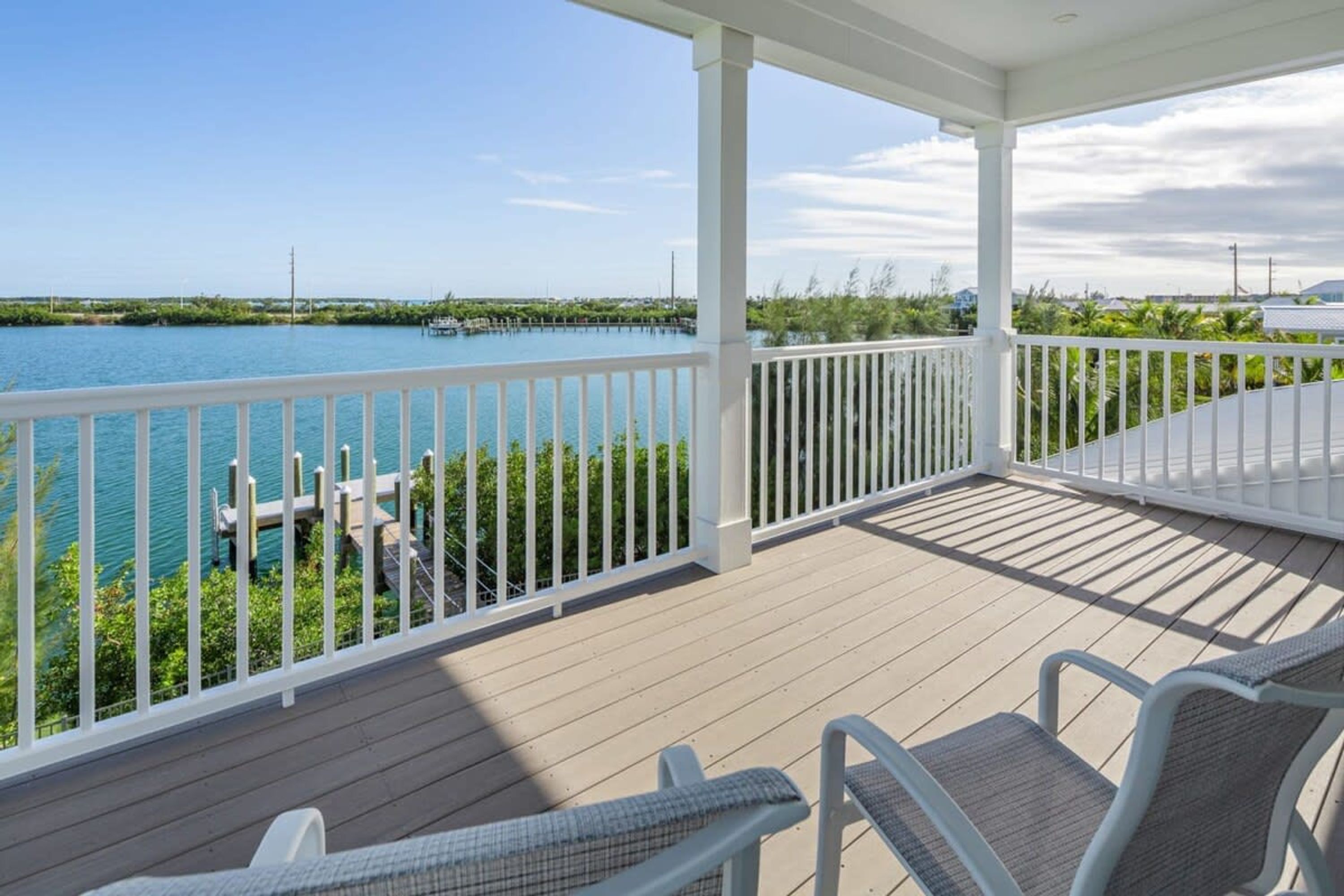 A covered deck with white railings overlooking a body of water, dock, and greenery.