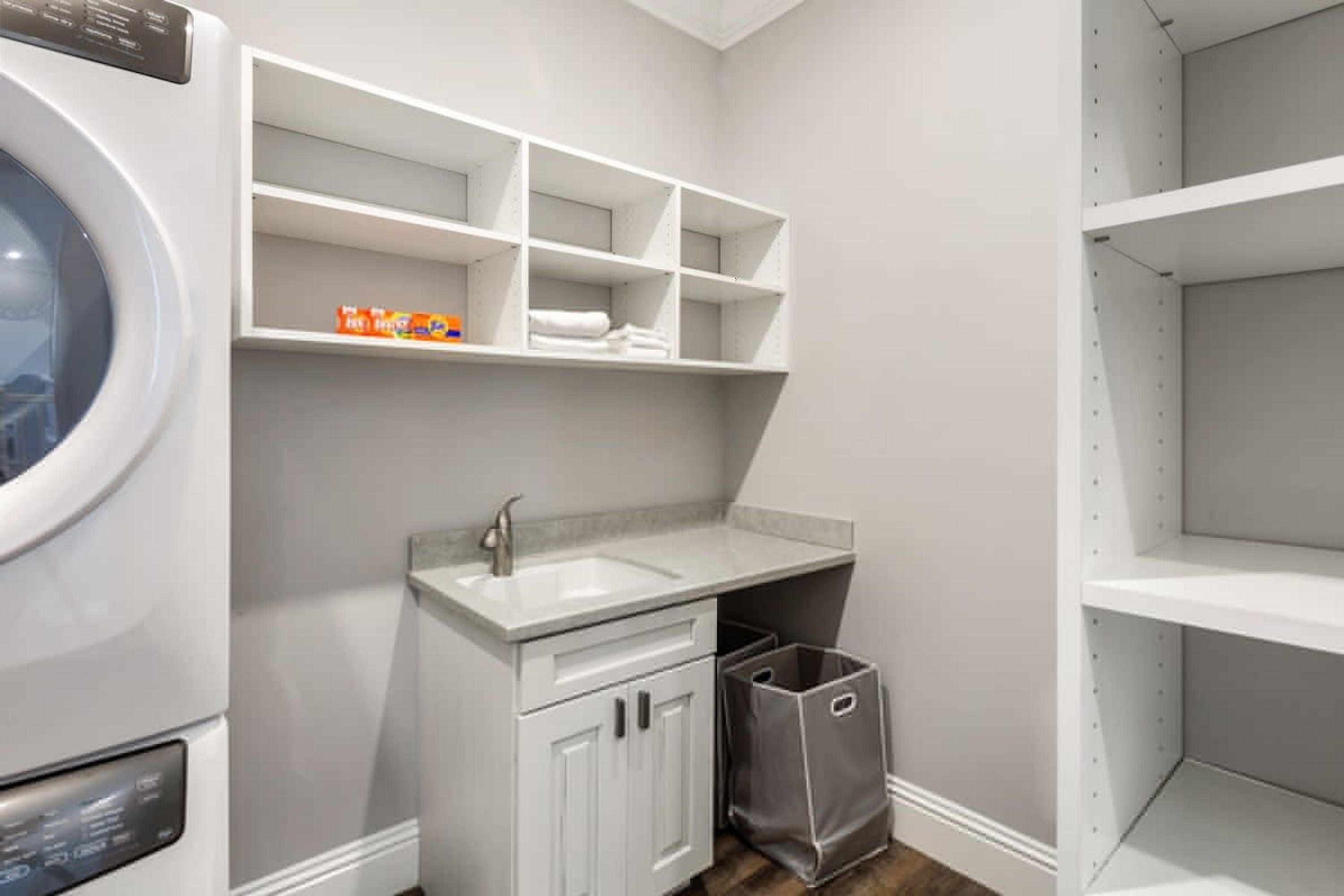 A laundry room with a washing machine, a sink, and shelves above the counter.